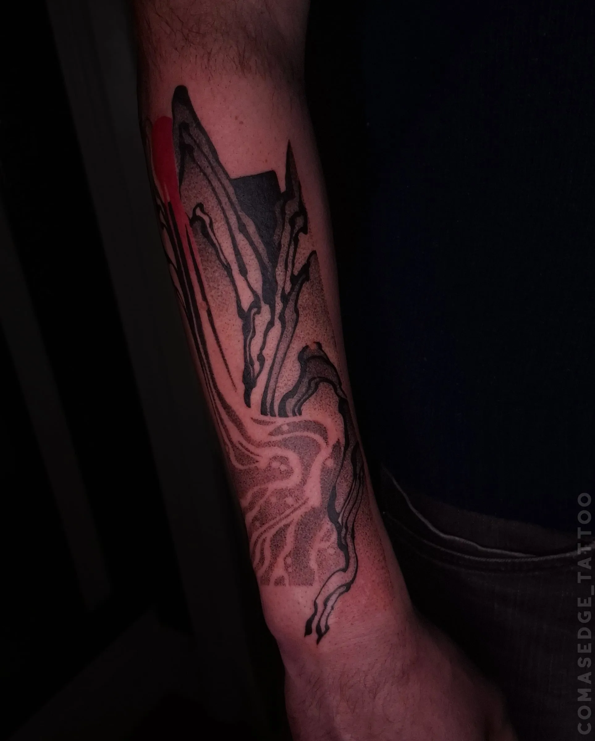 Tatouage en noir et rouge d’un paysage de montagnes et d’une rivière sur l’avant-bras, inspiré d’une estampe japonaise revisitée.