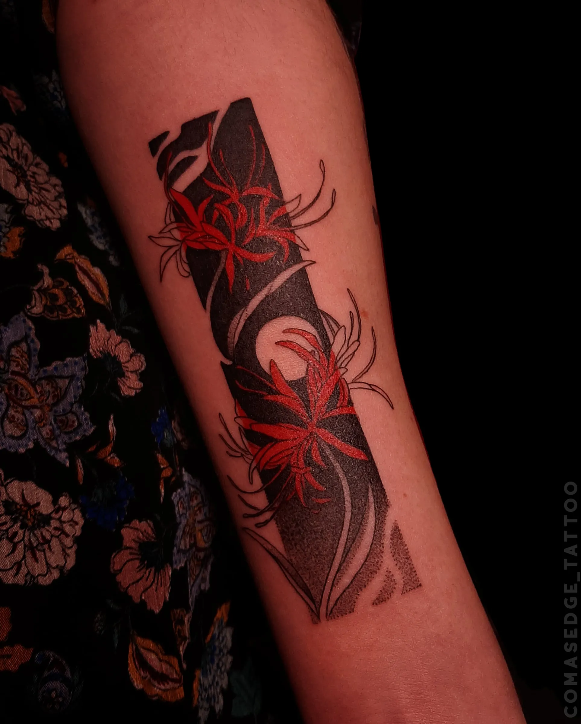 Tatouage de fleurs de lycoris rouges sur le biceps, intégrées à une composition verticale de formes noires anguleuses et d’un cercle clair.