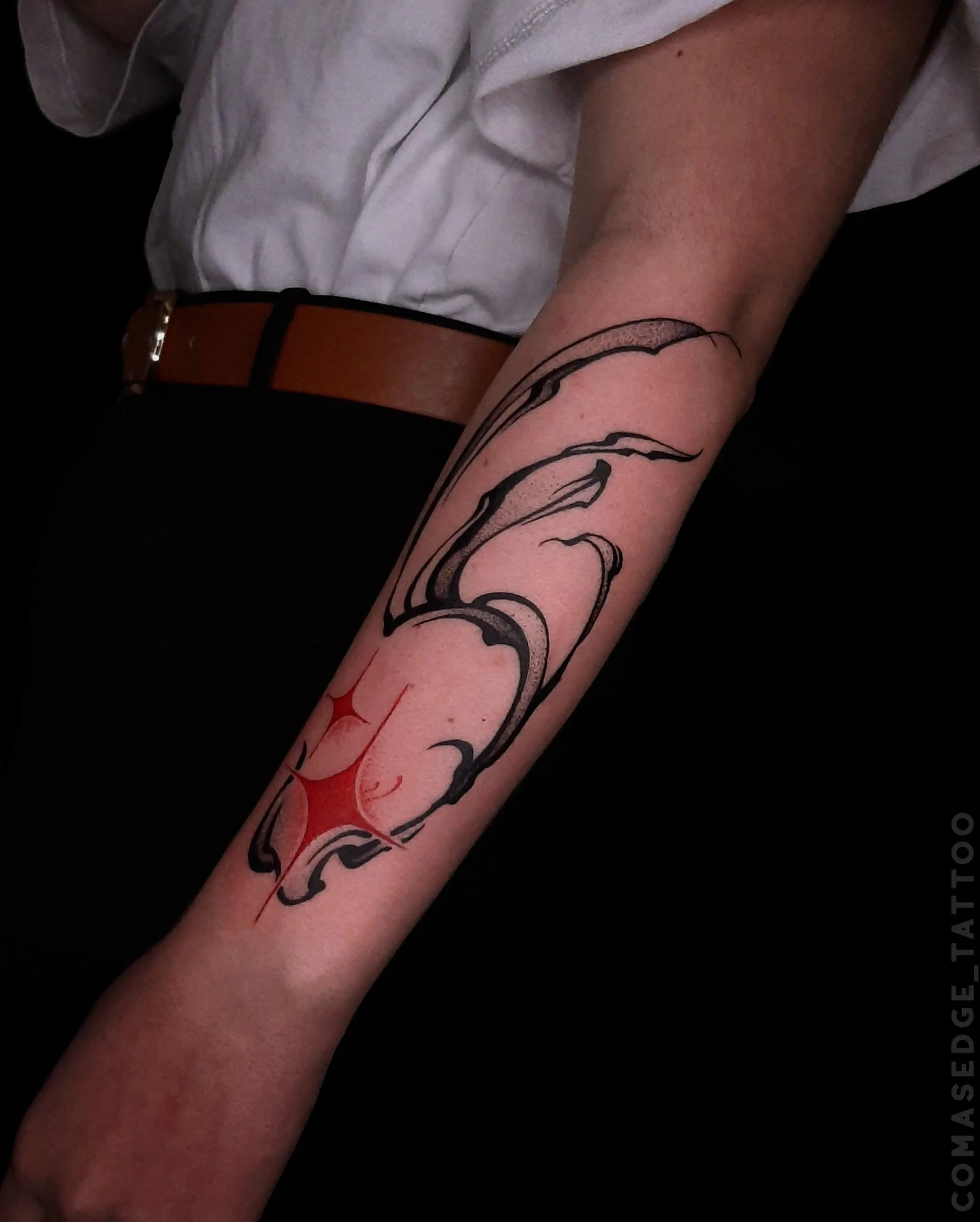 Tatouage abstrait noir sur l’avant-bras, composé de longues formes fluides et ponctué de scintillements rouges.