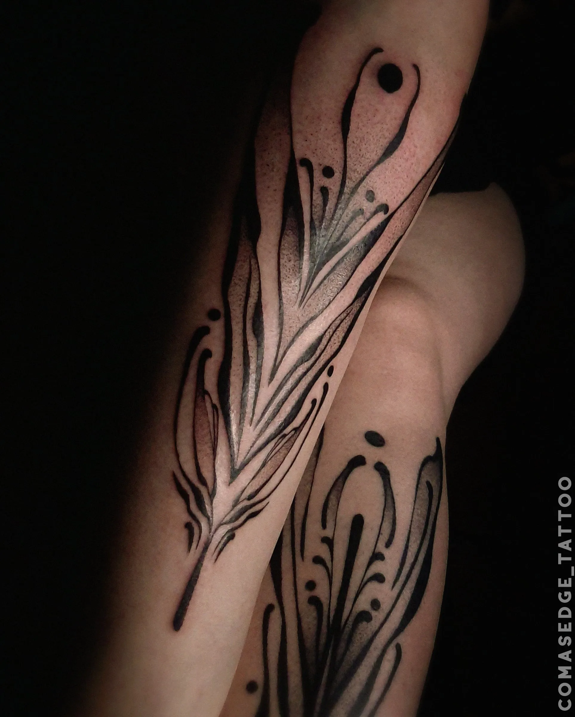Tatouages ornementaux noirs sur les tibias, composés de lignes fines, de contours graphiques et d’ombrages en dotwork.