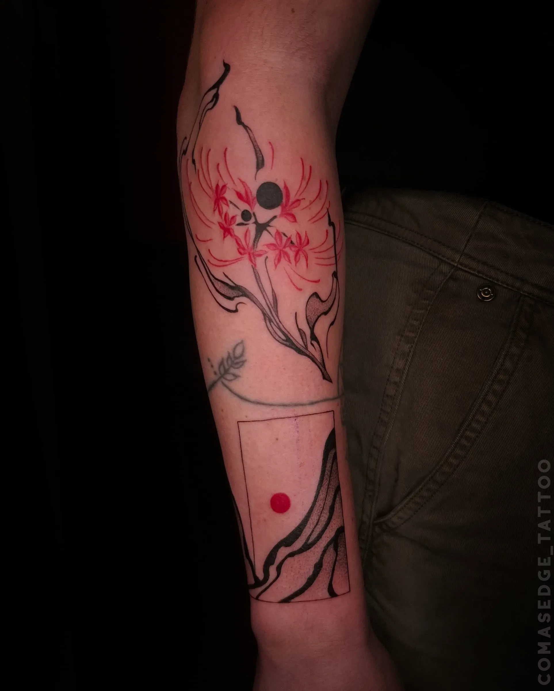 Tatouage noir et rouge sur l’avant-bras associant des fleurs de lycoris, des branches stylisées et des montagnes dans un cadre avec un disque rouge.