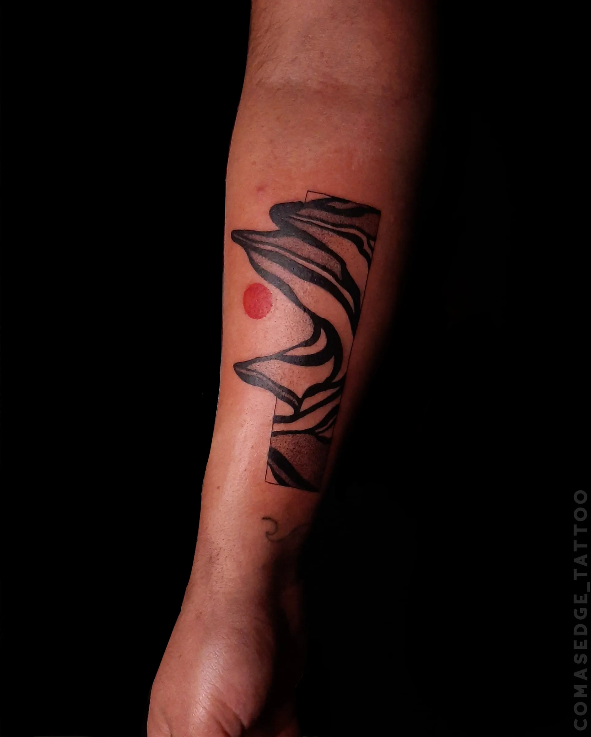 Petit tatouage rectangulaire abstrait noir sur l’avant-bras, composé de courbes graphiques et d’un disque rouge.
