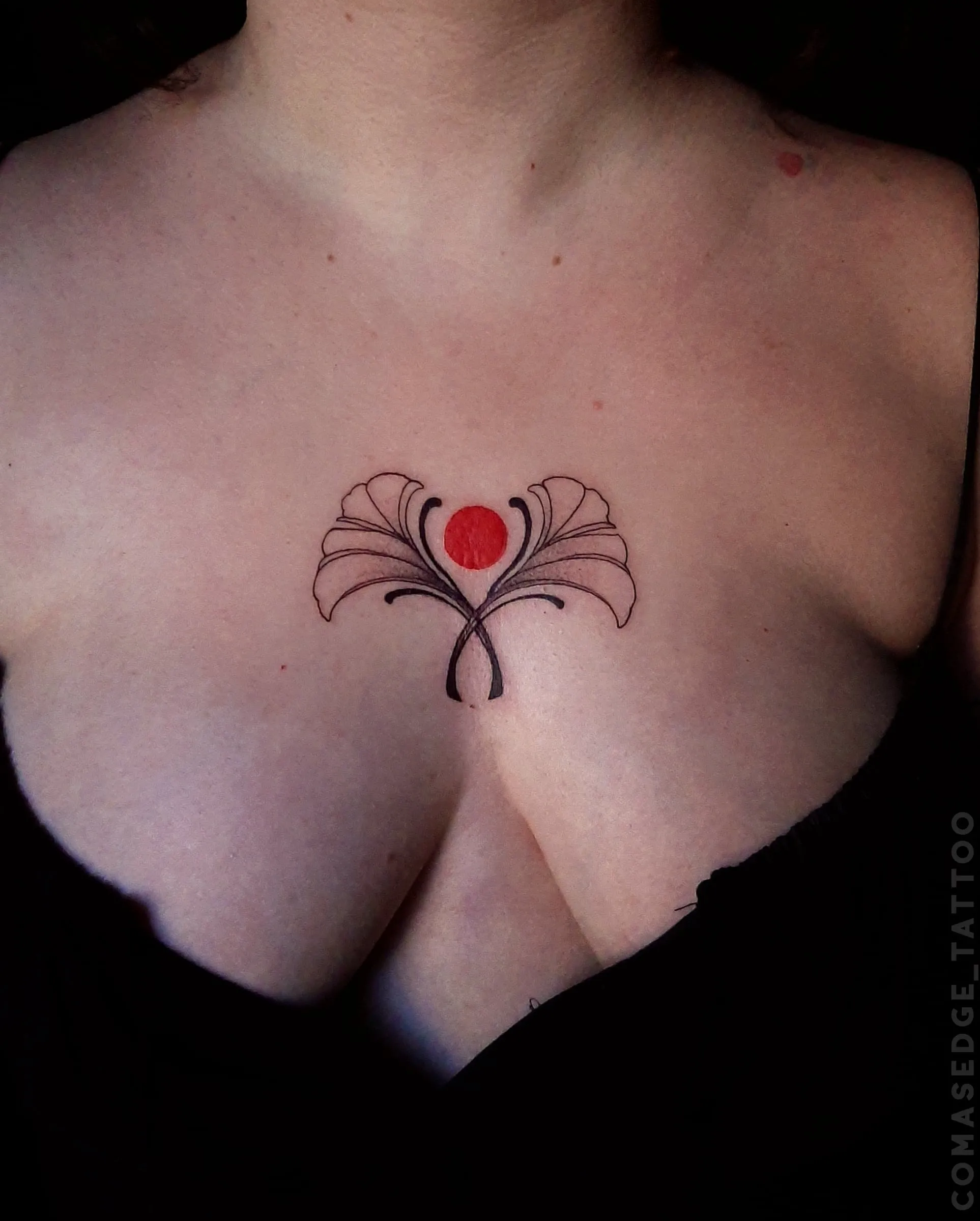 Tatouage symétrique de deux feuilles de ginkgo noires encadrant un cercle rouge, placé sur le sternum au centre de la poitrine.
