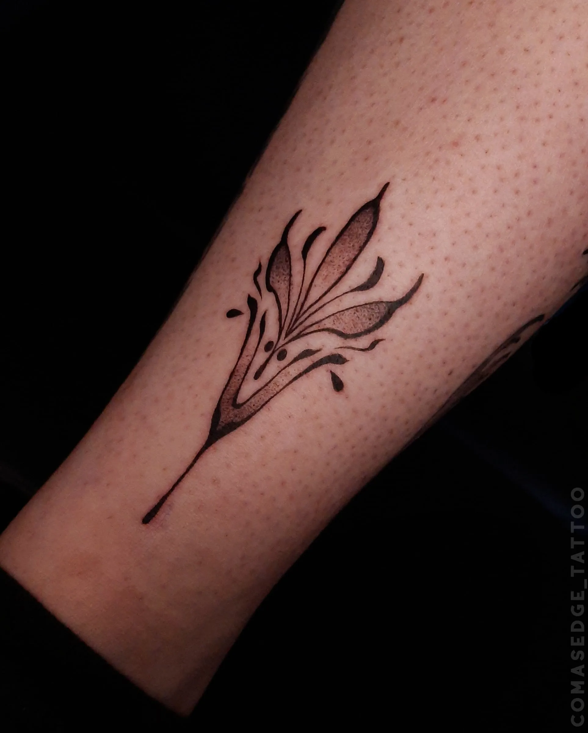 Petit tatouage fineline noir d’une fleur stylisée à la cheville, juste au-dessus du talon.
