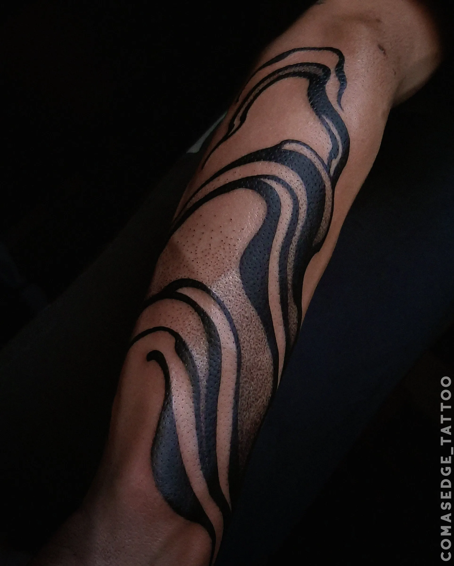 Tatouage suminagashi noir sur l’avant-bras, composé de courbes épaisses, fluides et superposées.